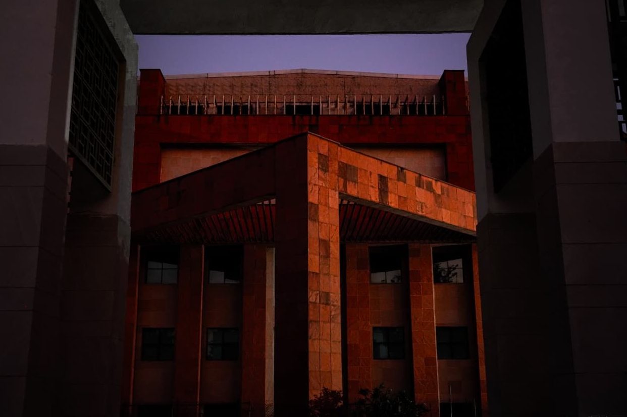 The red sandstone academic block silhouetted against a purple-orange dusk sky